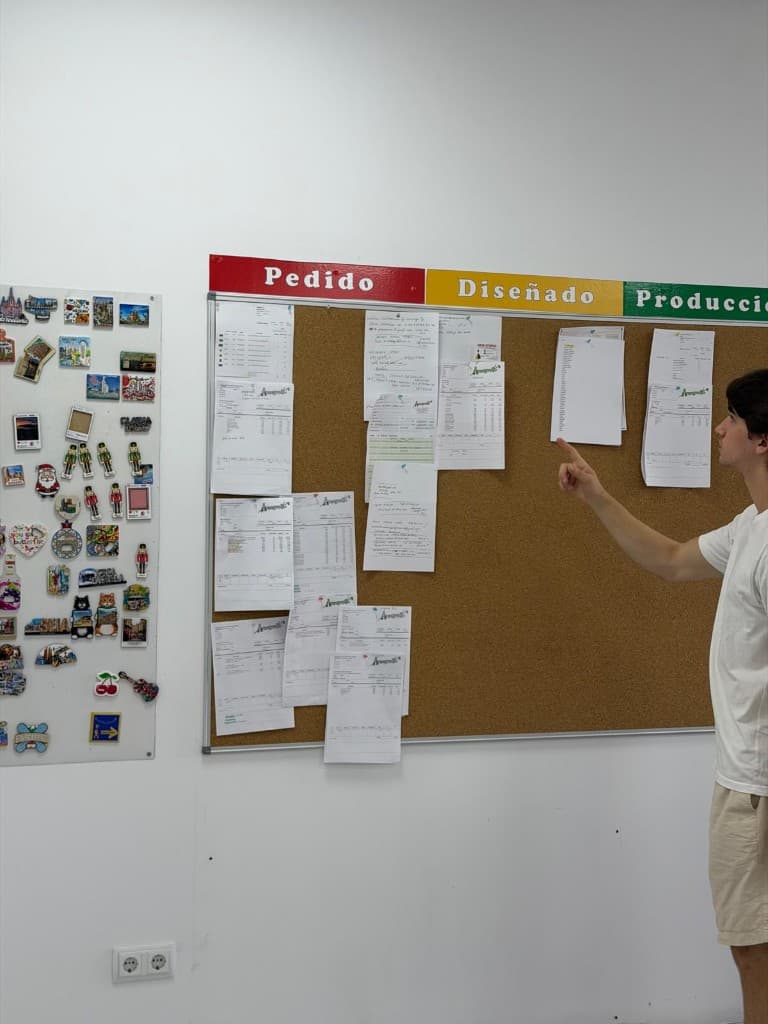 Pointing at a corkboard tracking orders through design and production